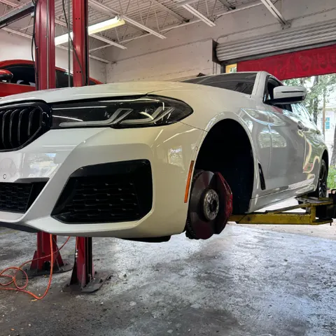 White BMW on a lift at AutoPlus with the wheel removed for brake service